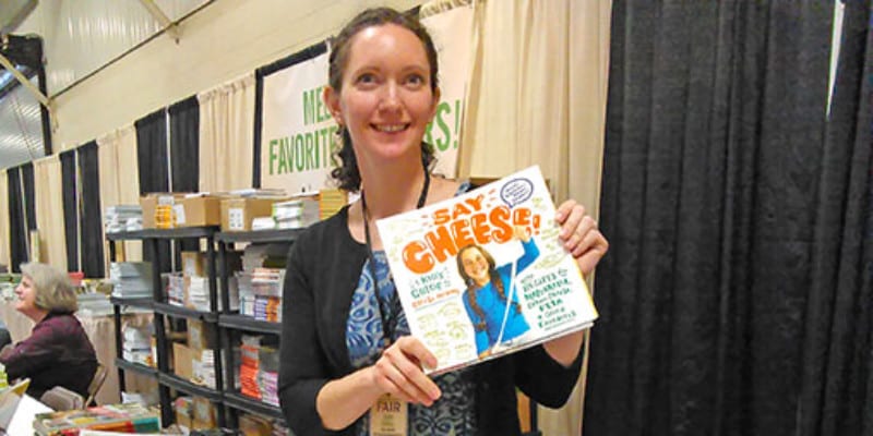 Woman holding up "Say Cheese" at a book signing