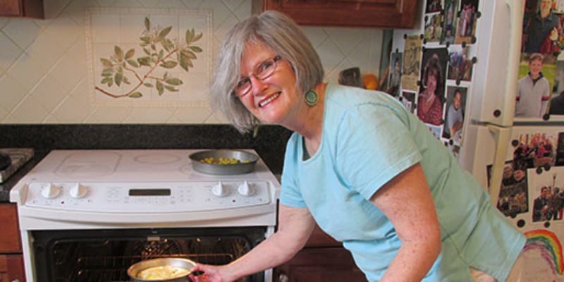 Woman smiling while pulling pan out of oven in kitchen
