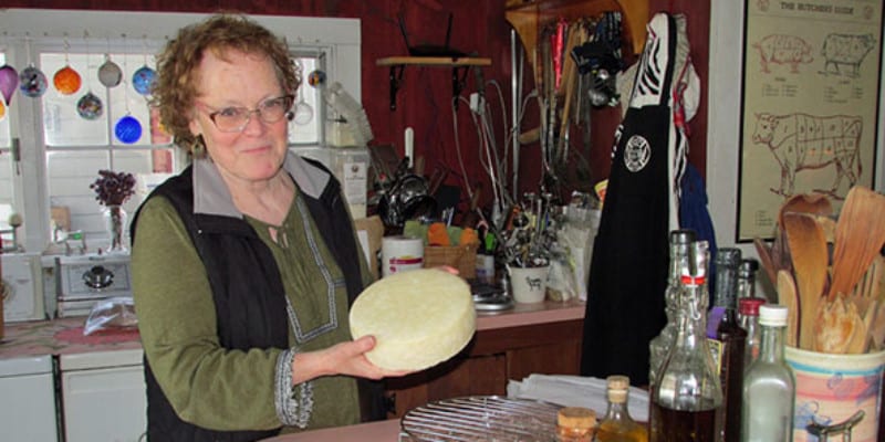 A woman holding a wheel of cheese in a kitchen