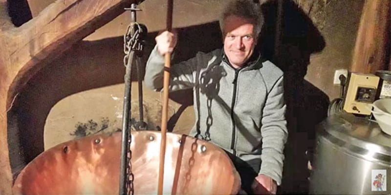 A screenshot of a man stirring something in a large copper vat