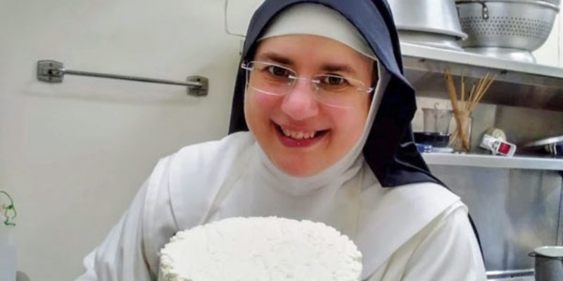 A nun holding a wheel of cheese.