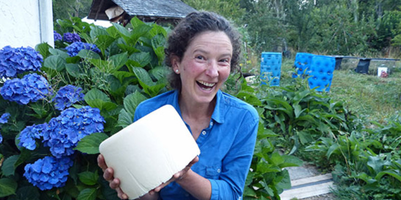 Lady smiling while holding block of cheese in backayard